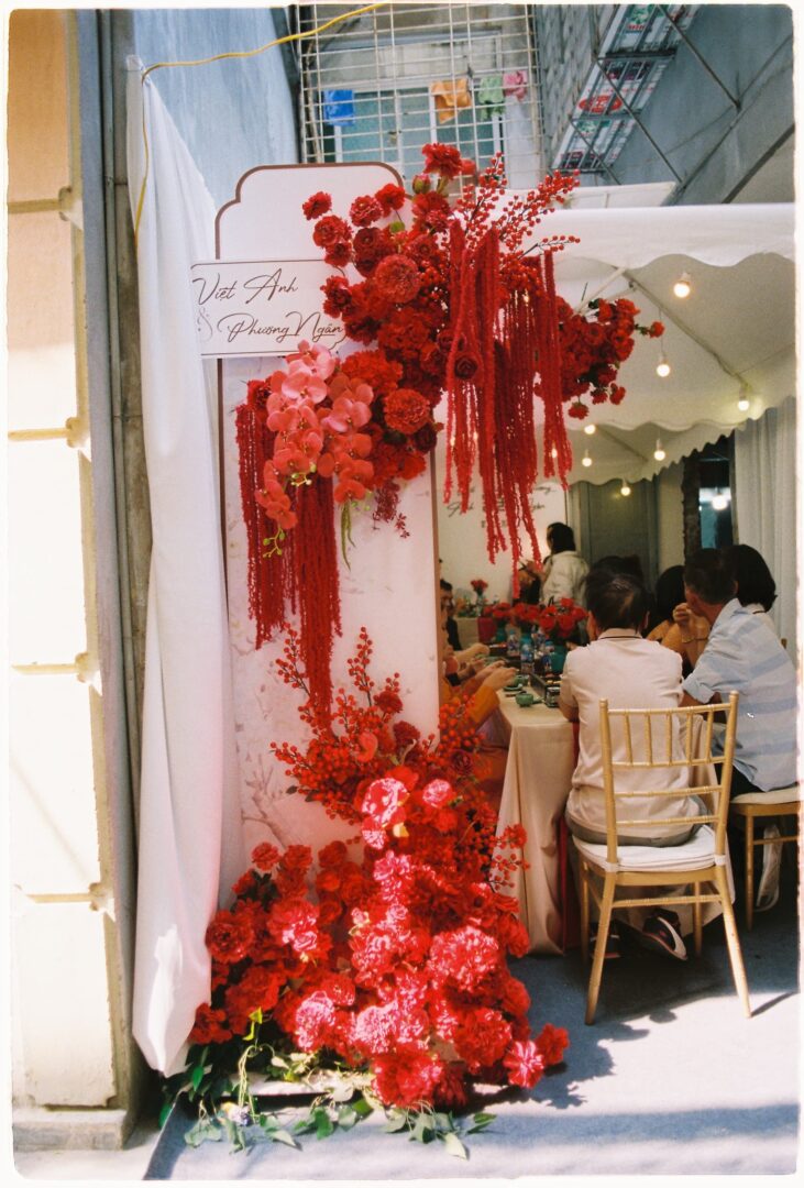 Wedding reception entrance decorated with cascading red flowers, leading to a banquet table where guests are seated under a canopy