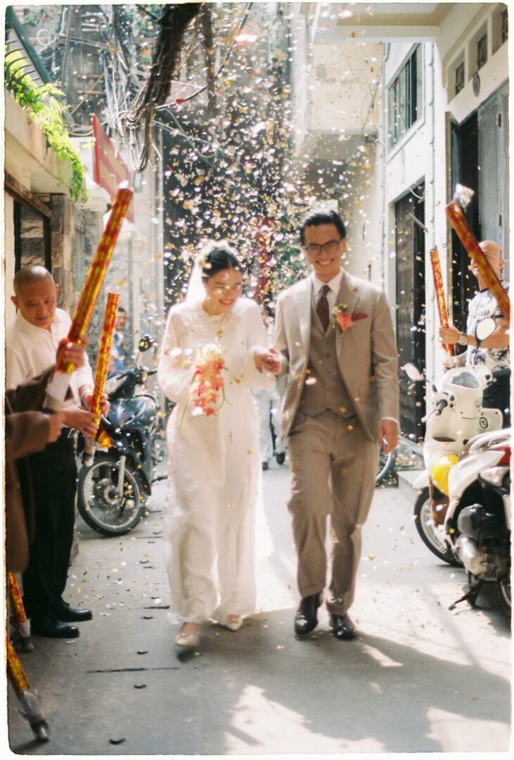 Bride and groom walking hand in hand down a narrow street as guests celebrate with confetti during their wedding exit