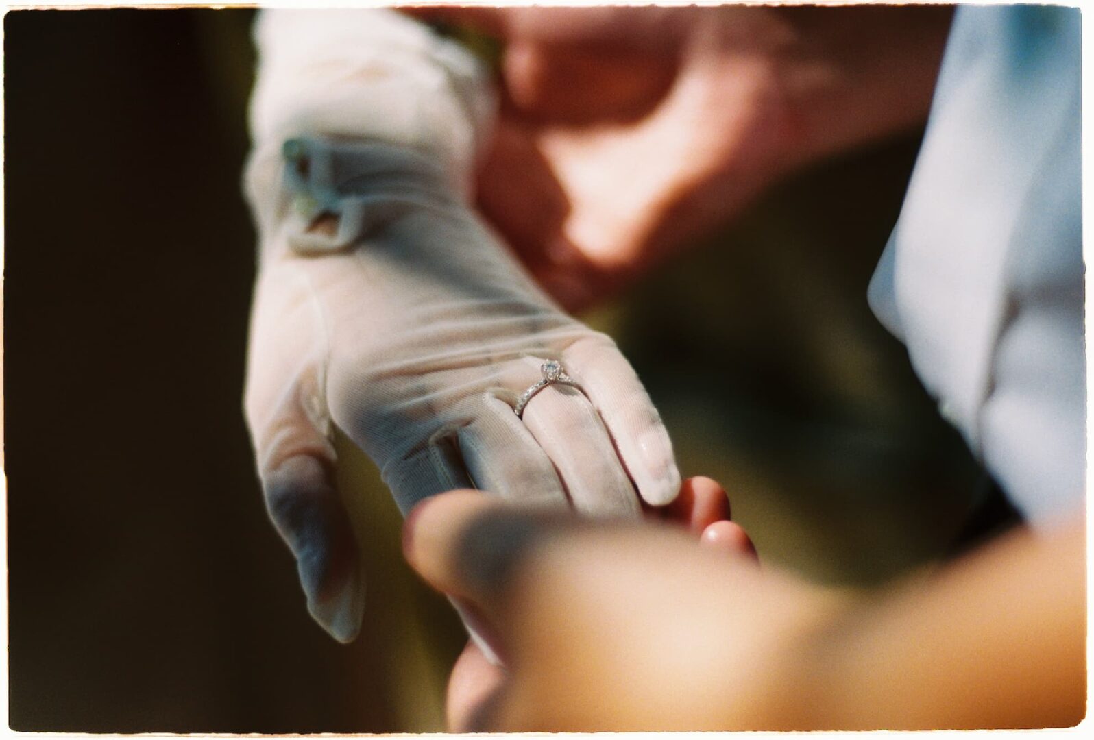 Close-up of the bride’s gloved hand wearing a wedding ring while holding the groom’s hand in soft natural light