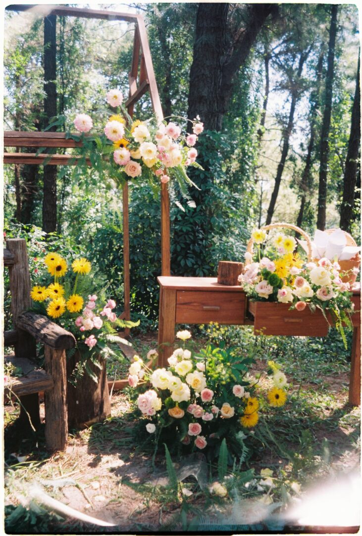 Outdoor wedding ceremony setup in a forest, featuring wooden furniture and abundant floral arrangements in soft pastel colors