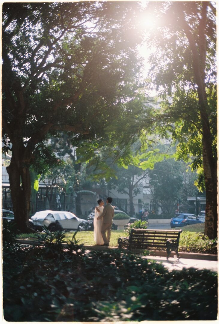 Bride and groom walking together through a city park, surrounded by trees and soft morning sunlight